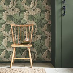 a wooden chair sitting in front of a green wallpapered room with a rug on the floor