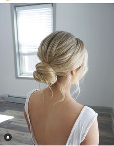 a woman with blonde hair in a white top is looking out the window and has her back to the camera