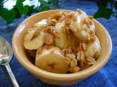 a bowl filled with sliced bananas next to a spoon on a blue table cloth and green leaves in the background