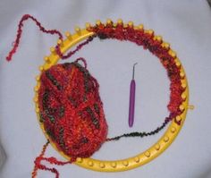 a red ball of yarn sitting on top of a yellow circular frame next to a knitting needle