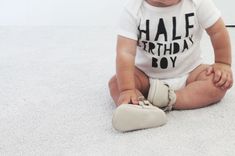 a baby sitting on the floor wearing a shirt that says half birthday boy with shoes