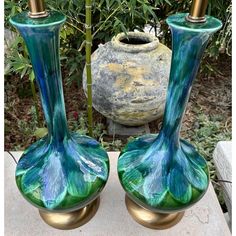 two green vases sitting next to each other on top of a cement slab in front of some bushes