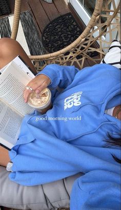 a woman reading a book while sitting on a chair with a cup of coffee in her hand