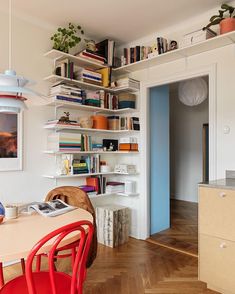 a dining room table with red chairs and bookshelves