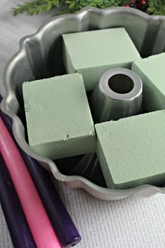 there is a cake pan with green squares in it and two pink sticks next to it