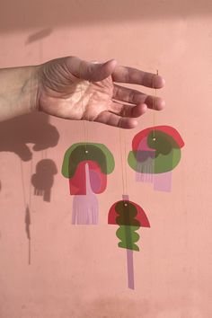 a person's hand reaching for some paper art hanging from the ceiling in front of a pink wall