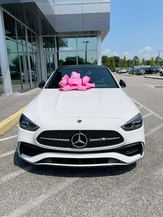 a white car with a pink bow on it's hood parked in front of a building