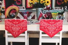 two red bandanas sitting on top of white chairs in front of a table with yellow flowers