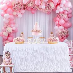 a table topped with pink and white balloons next to a baby cake on top of a table