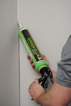 a man holding a green and white glue on a wall with a screwdriver