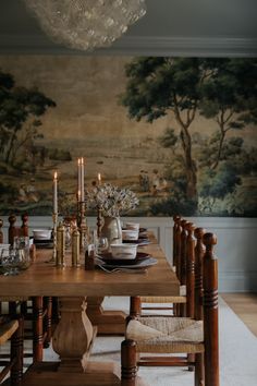 a dining room table with candles and plates on it in front of a wall painting