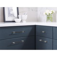 a vase with flowers on top of a counter next to a sink and cabinets in a kitchen