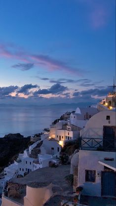 the sky is blue and pink at dusk over some white buildings with lights on them