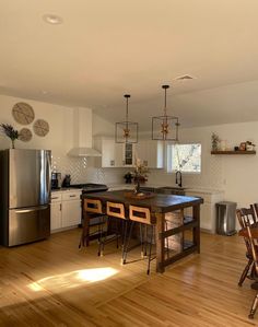 a kitchen with wooden floors and white walls, has an island table surrounded by chairs