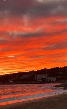 an orange and red sunset over the ocean with buildings on the shore line in the distance