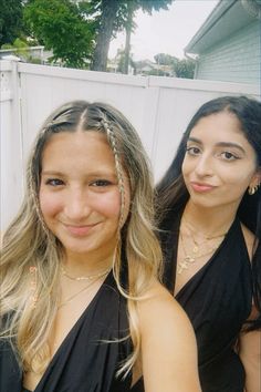 two young women standing next to each other in front of a white fence and house