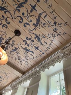 an ornately painted wooden ceiling in a room with two windows and a light fixture