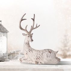 a deer figurine sitting next to a lantern on a snowy surface with snow flakes