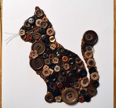 a cat made out of buttons sitting on top of a piece of white paper next to a wooden frame