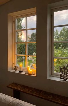 two candles are lit in front of a window with the view of a garden outside