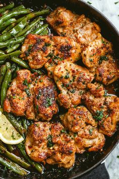 chicken and green beans in a skillet with lemon wedges