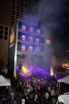 a large group of people standing in front of a tall building with lights on it