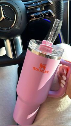 a person holding a pink tumbler in their hand while sitting next to a steering wheel