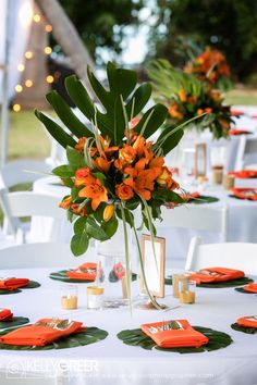 an arrangement of orange flowers and greenery on a white table cloth with place settings