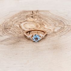 an engagement ring with a blue topaz sits on a piece of wood