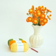 a white vase filled with orange flowers next to a crochet ball and yarn