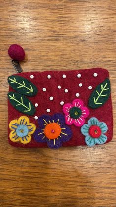 a red purse with flowers on it sitting on a wooden table next to a button