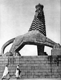 two women are walking past a large lion statue in the middle of a brick wall