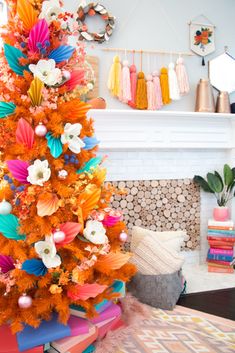 an orange christmas tree decorated with colorful paper flowers and pom - poms in front of a fireplace