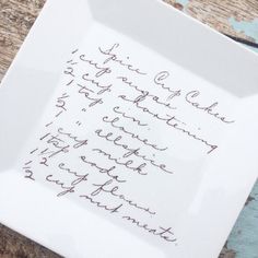 a white plate with writing on it sitting on top of a wooden table next to a knife