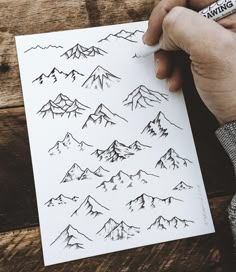 a person is drawing mountains on a piece of paper