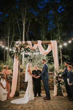 a bride and groom are getting married under an outdoor wedding arch with lights strung over it