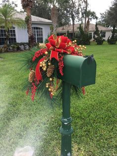 a green mailbox decorated with red and gold christmas decorations, pine cones and bows