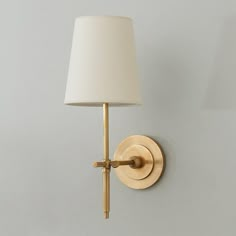 a wall light with a white shade on it's side and a gold arm