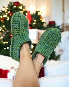 a woman's feet wearing green knitted slippers in front of a christmas tree