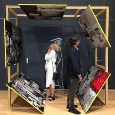 two people standing in front of an art display with various pieces of artwork on it