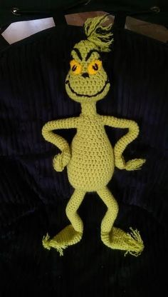 a crocheted frog is posed on a black surface with yellow eyes and hair