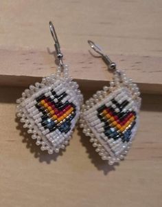 the beaded heart earrings are hanging from hooks on a wooden surface, with beads attached to them