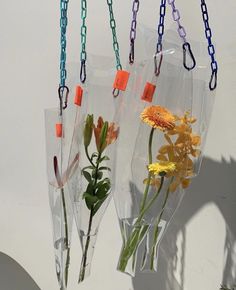 three clear vases with flowers in them hanging from chains on a wall, one is empty and the other has yellow flowers