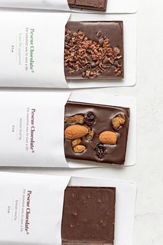 three bars of chocolate with nuts and cranberries on top are lined up next to each other