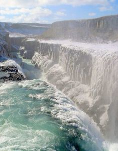 the water is green and blue as it pours into the river from the cliffs