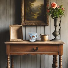 a painting and vase on a table in front of a wooden paneled wall with an old - fashioned frame