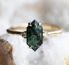 a green diamond ring sitting on top of a rock