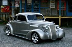 an old silver car parked in front of a building with signs on the side of it