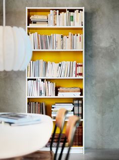 a book shelf filled with lots of books next to a dining room table and chairs