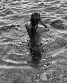 a woman is sitting in the water with her hand on her head and looking back